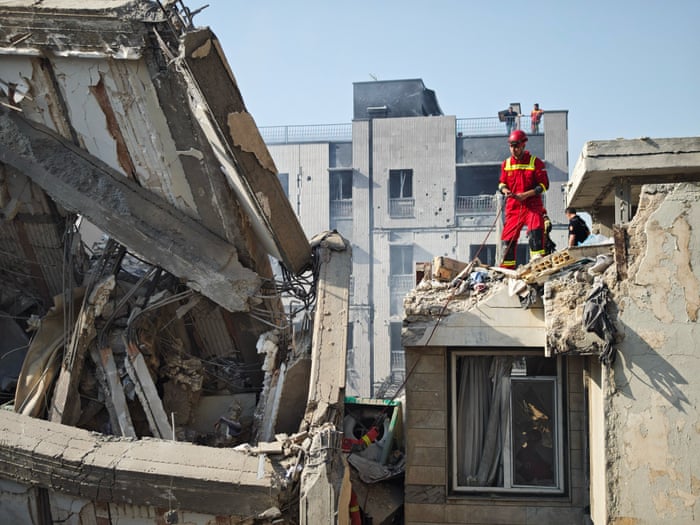 Rescue workers among damaged buildings after June 2025 Israeli strikes, in the selected Guardian report